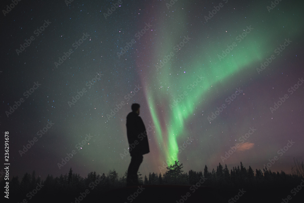man standing and watching Northern light / Aurora borealis in the sky of finland during winter