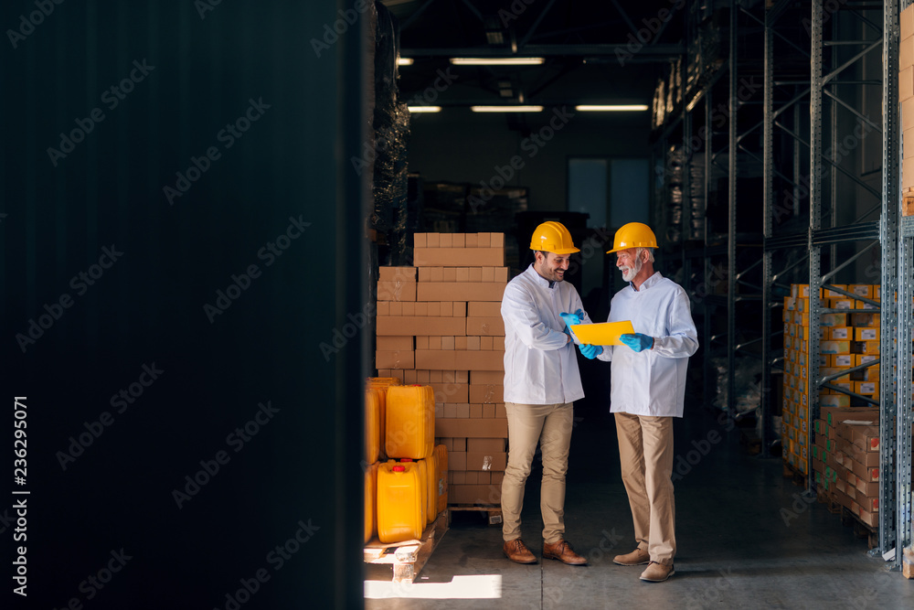 Two man discussing while standing in warehouse. Senior holding documents. Two man discussing while standing in warehouse. Senior holding documents.