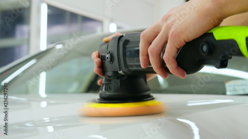 Closely shown as a professional worker polishes the transport (car) body using a polishing tool (machine). Concept from: Auto service, Car Painting, Machine washing.