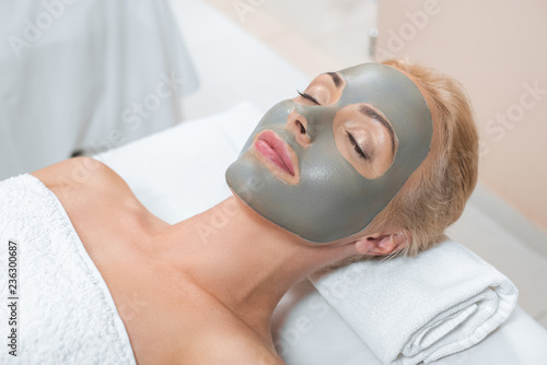 close up of blonde woman lying with facial clay mask in spa