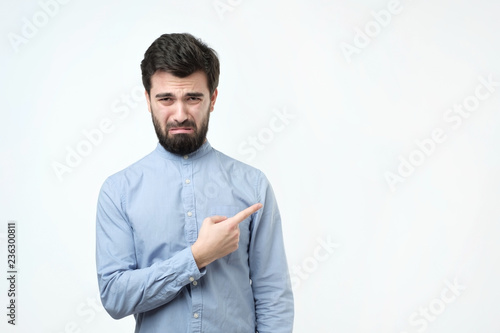 Fotografie Sad gloomy european boyfriend, whining or crying, frowning and trying to hide tears pointing with finger aside