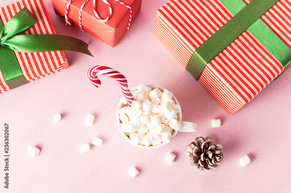 Obraz premium White mug with marshmallows Candy Cane gifts boxes with green ribbon on pink background Flat Lay Winter traditional drink food Festive decor. Christmas New Year presents Xmas holiday