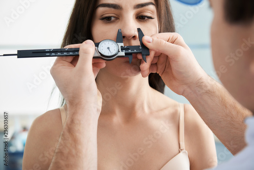 Doctor measuring proportions of female nose while using calipers