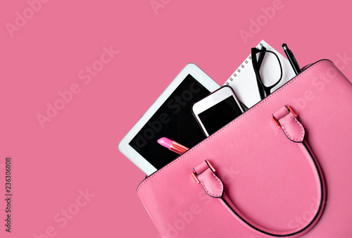 Business woman's everyday-life travel accessories flat lay on pastel pink background with formal pastel pink handbag, a cellphone, blank notepad, luxury pen, glasses and lipstick, copy space for text