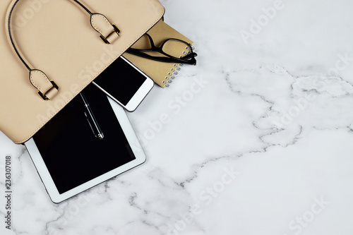 Business woman's everyday-life travel accessories flat lay on white marble background with formal beige handbag, a cellphone, blank notepad, luxury pen, glasses and lipstick with copy space for text