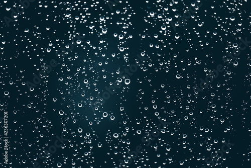 Dirty window glass with drops of rain. Atmospheric blue background with raindrops. Droplets and stains close up. Detailed transparent texture in macro with copy space. Rainy weather.