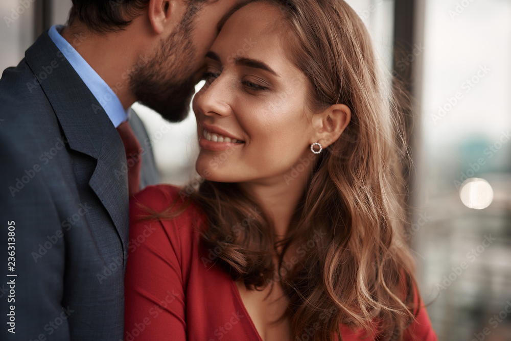 Concept of romantic date. Close up portrait of happy beloved lady clinging with love to her male lover while standing in his arms on balcony Concept of romantic date. Close up portrait of happy beloved lady clinging with love to her male lover while standing in his arms on balcony