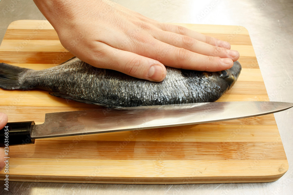 Chef's hand cutting fish into thin slices with a knife.Fish fillet on a  wooden cutting board. Stock Photo