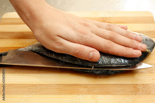 Chef's hand cutting fish into thin slices with a knife.Fish fillet on a wooden cutting board.