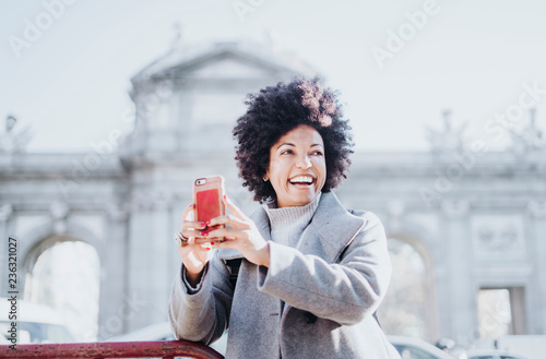 Portrait of attractive afro woman using mobile phone in Madrid, Spain. Puerta de Alcala.