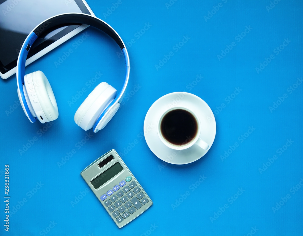 Headphones, tablet, calculator and coffee cup on a blue background. Headphones, tablet, calculator and coffee cup on a blue background.