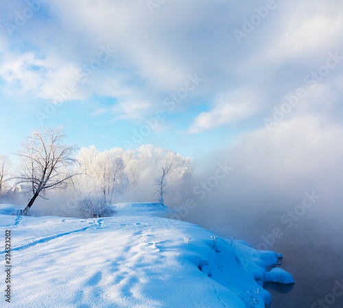 Winter landscape of trees and river in a foggy morning. Frost and cold and sunshine.