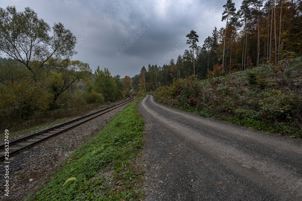 Fototapeta premium forest path next to train tracks under storm clouds in autumn