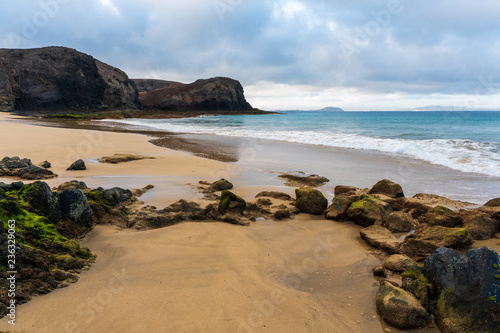 The Wax Beach (Playa de la Cera) tourist attraction in Lanzarote, Canary Islands, on a beautiful summer morning. Empty beach with volcanic rocks, golden sand and clear turquoise water.