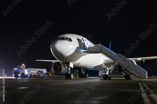 Wide-body passenger airplane with boarding stairs at the night airport apron. Aircraft ground handling