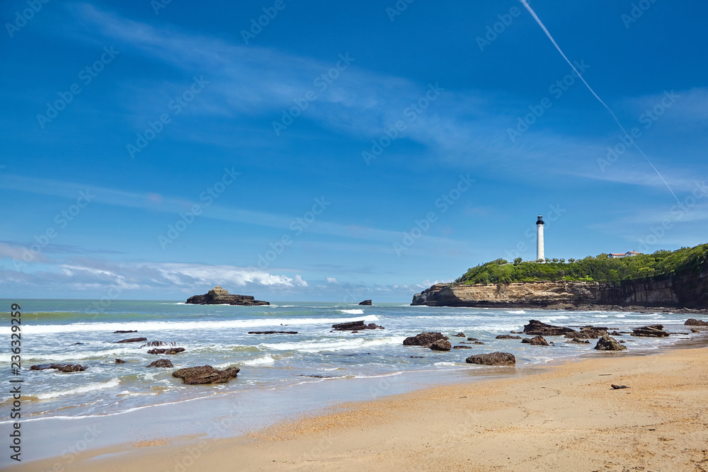 Biarritz, France. Sand beach, lighthouse, rocky shore of the ocean.  Bay of Biscay, Atlantic coast, Basque country. Sunny summer day with blue sky.