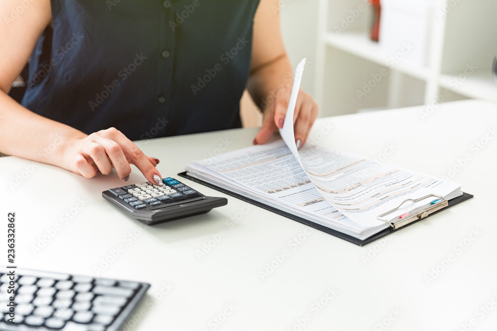 Women's hands count on the calculator and fill out the form. Women's hands count on the calculator and fill out the form.