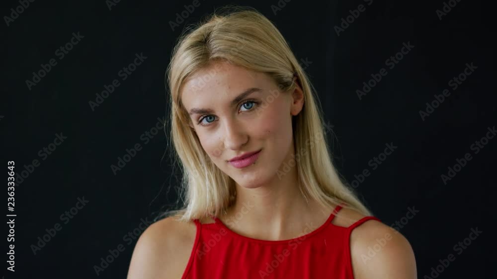Beautiful young woman in red garment looking at camera while standing on black background Beautiful young woman in red garment looking at camera while standing on black background