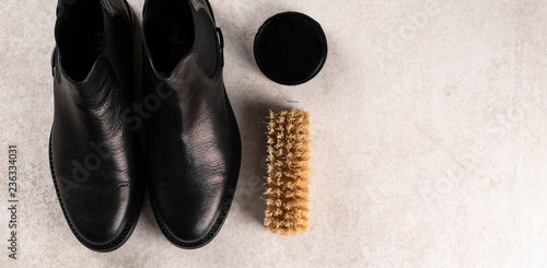 black leather boots, shoe polish and a brush on light marble surface