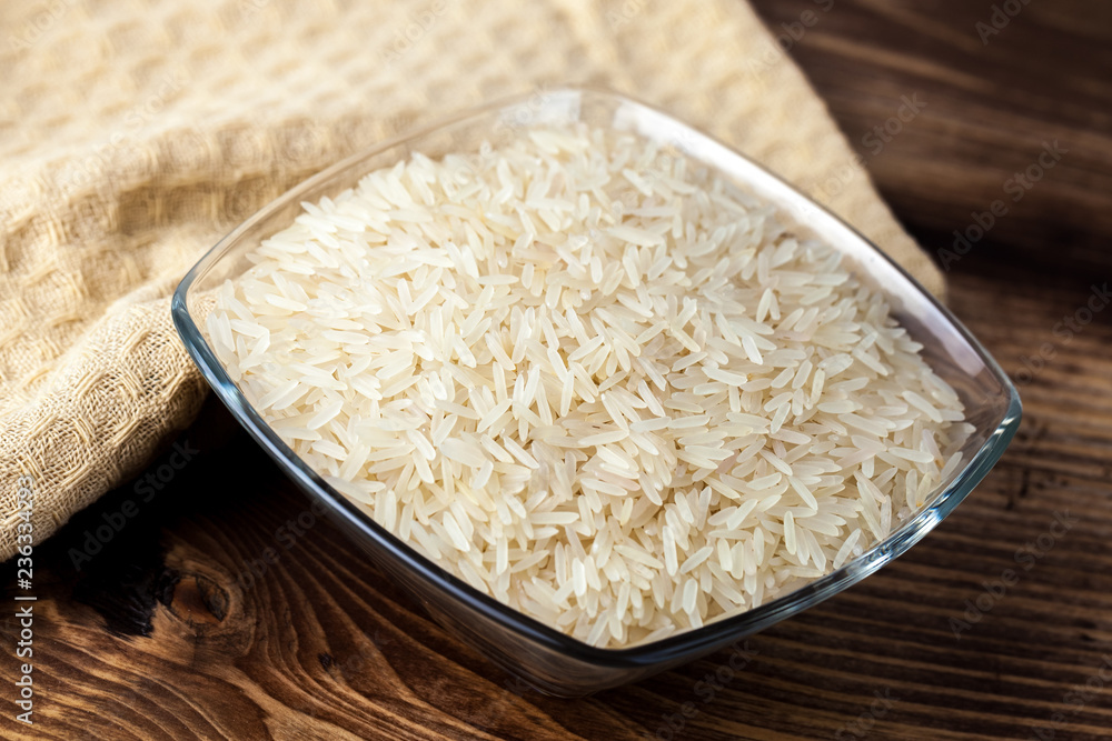 Seeds of white rice in glass bowl on wooden table, ingredient for cooking Seeds of white rice in glass bowl on wooden table, ingredient for cooking