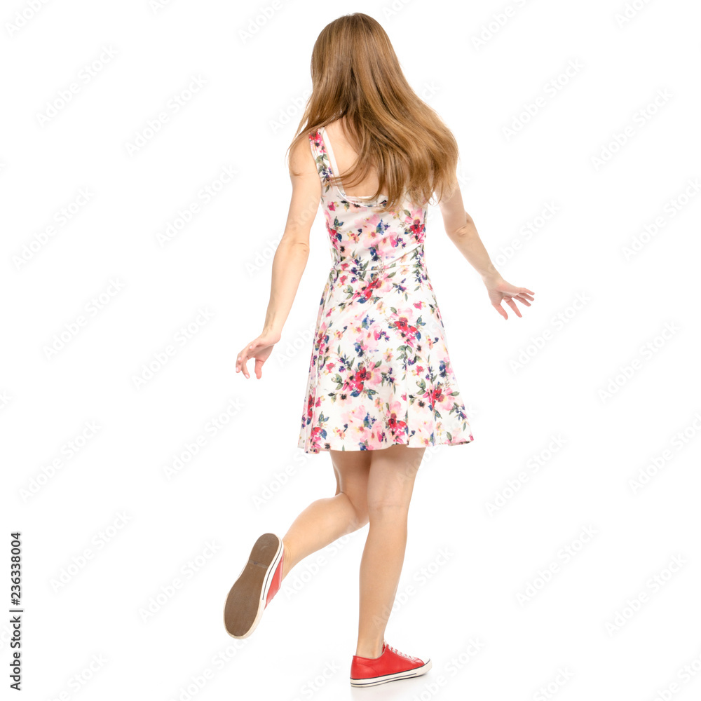 Beautiful woman in dress with flowers print and sneakers showing of positive emotions goes happy back view on white background isolation Beautiful woman in dress with flowers print and sneakers showing of positive emotions goes happy back view on white background isolation