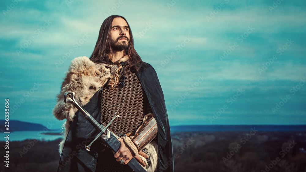 Obraz premium Long haired knight with the two-handed sword. Panoramiс view on the background.