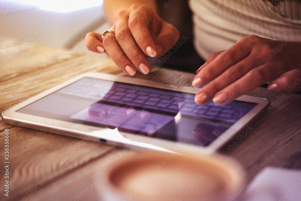 young woman works with digital tablet on a background of cup of coffee on a wooden table young woman works with digital tablet on a background of cup of coffee on a wooden table
