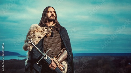 Long haired knight with the two-handed sword. Panoramiс view on the background.
