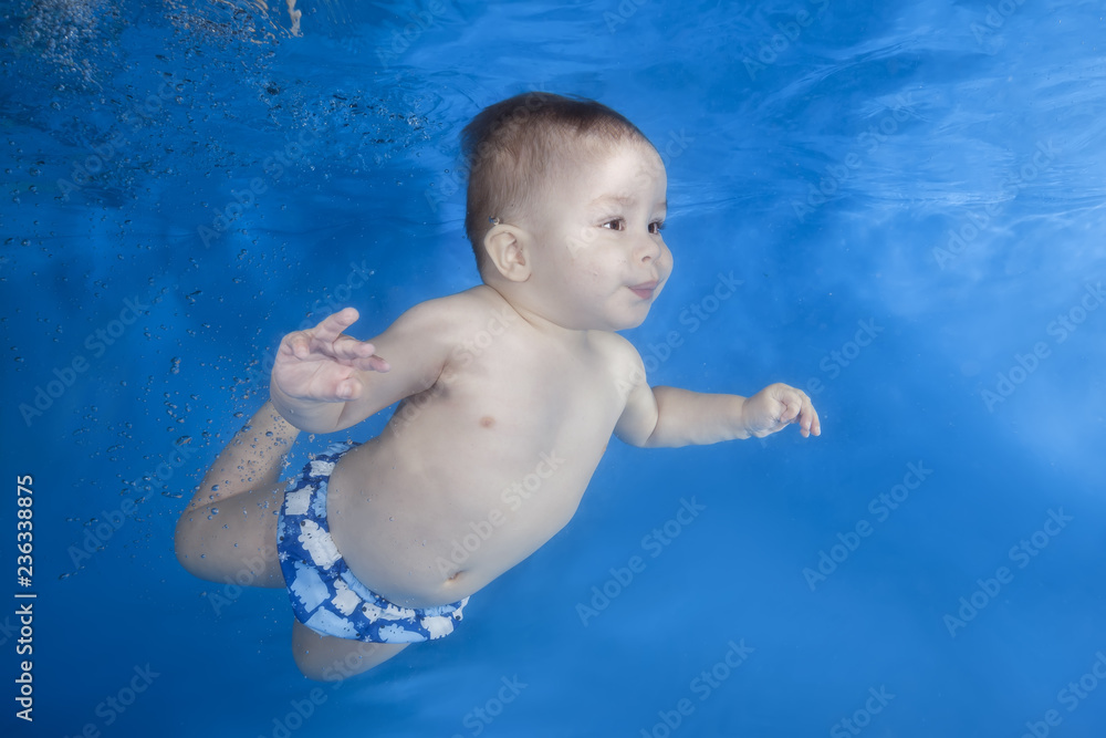 Boy swim underwater in the swimming pool on a blue water background. Healthy family lifestyle and children water sports activity. Child development, disease prevention