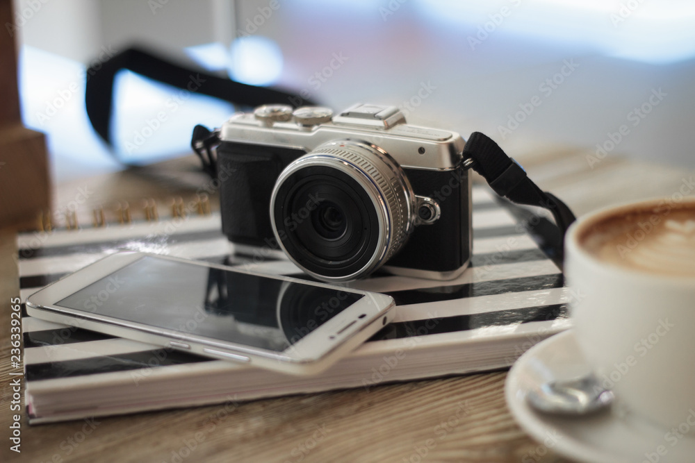 Compact digital photo camera on a wooden table with cup of coffee. Simple composition, soft focus