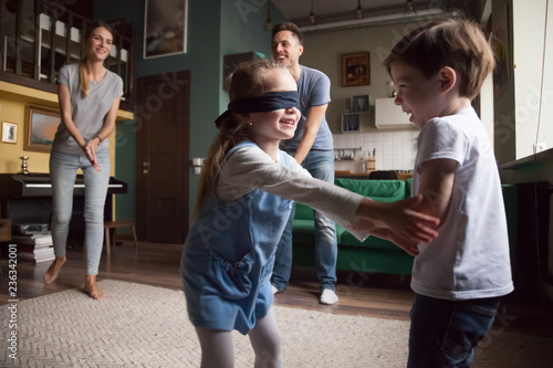 Young large family with two children playing hide-and-seek, little girl with blindfold caught boy, sister and brother playing together, family spending time together photo