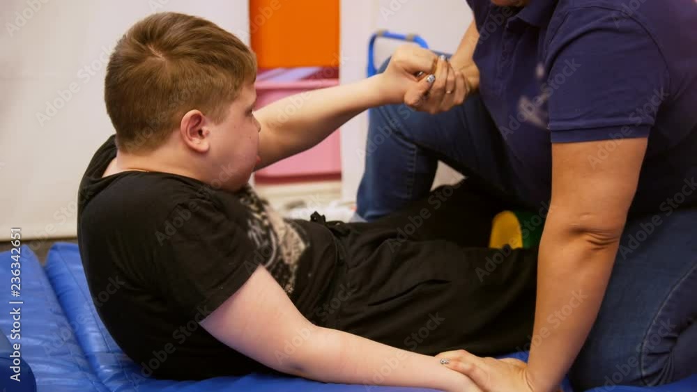 Medical centre. A woman doctor helps a kid with cerebral palsy disease to get up. Doing exercises on the back Medical centre. A woman doctor helps a kid with cerebral palsy disease to get up. Doing exercises on the back