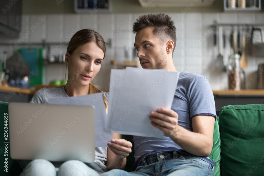 Upset man and woman sitting together on sofa, using laptop, wife and husband checking documents, reading bad news, financial problem, credit, loan, mortgage, bankruptcy Upset man and woman sitting together on sofa, using laptop, wife and husband checking documents, reading bad news, financial problem, credit, loan, mortgage, bankruptcy