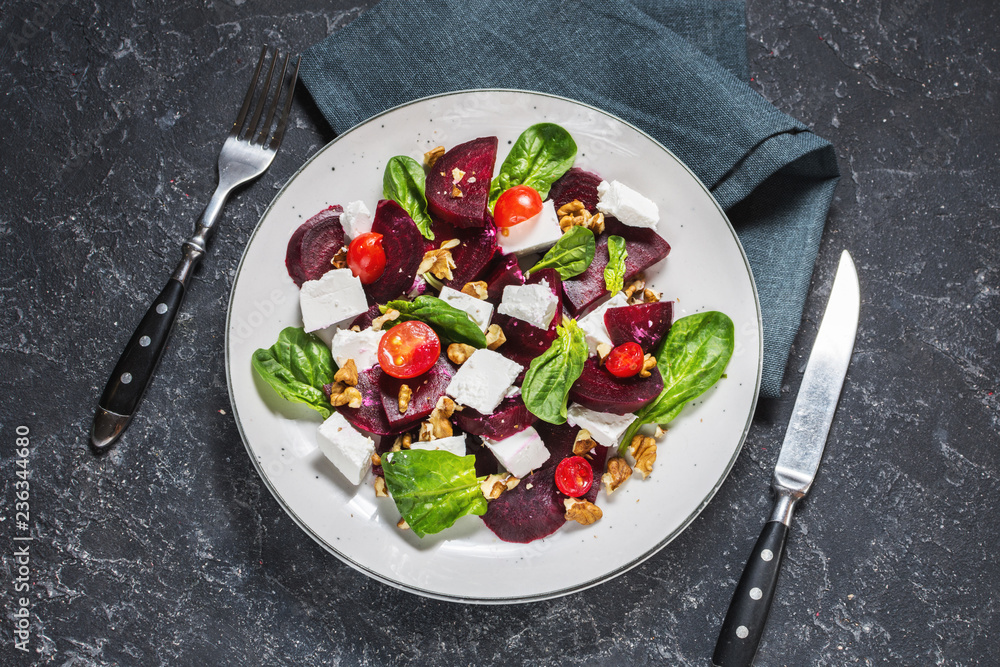 dish with a salad of feta, beetroot, cherry tomatoes and walnuts on a stone background