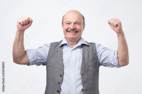 Portrait of happy spanish senior man with fists up celebrating his victory. Great news ever.