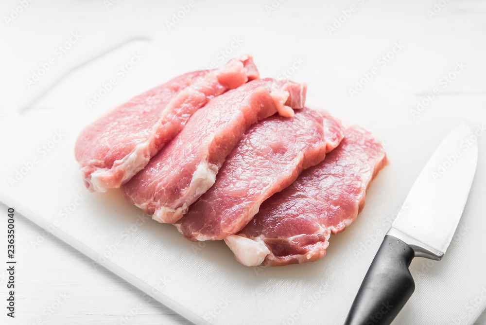 Sliced pork on white board and knife on white table