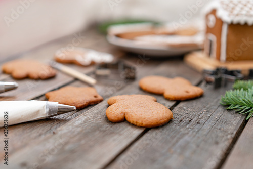 Fototapeta Naklejka Na Ścianę i Meble -  A tube of white icing. A lot of ginger biscuits in different form on brown wooden table. Decorated with white sweet glaze. Christmas mood, winter morning. Fir branches