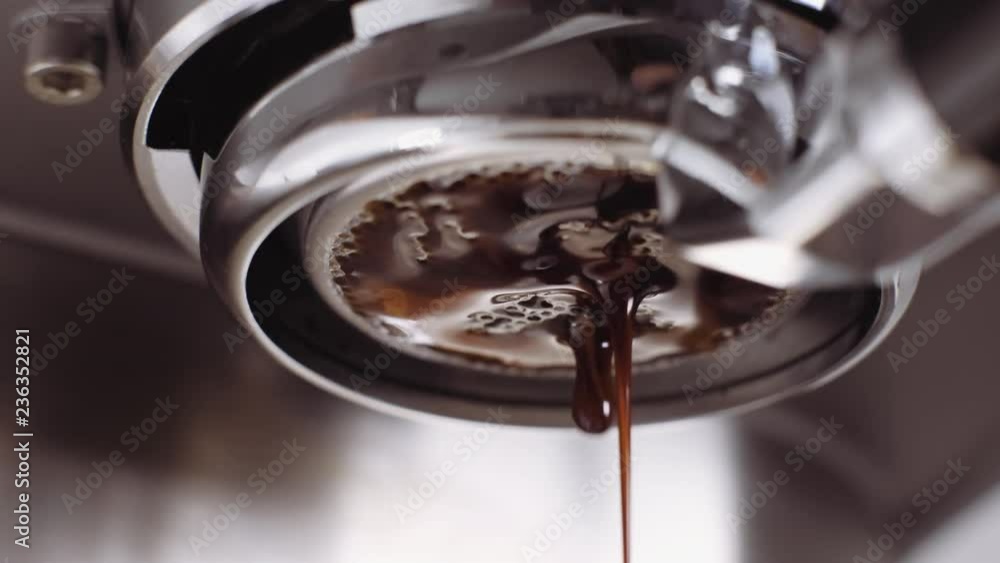 Pouring coffee stream from professional machine in cup. Barista man making double espresso, using filter holder. Flowing fresh ground coffee. Drinking roasted black coffee in the morning.