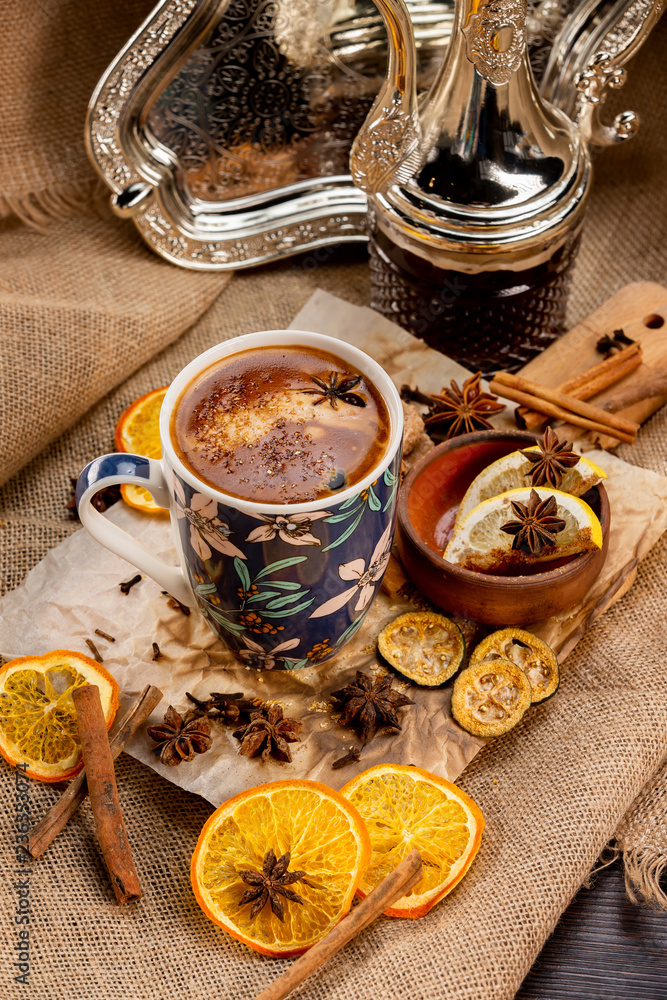 Closeup cup of turkish spiced coffee at decorated wooden table with orange chips, cennamon sticks and sack clothing background. Closeup cup of turkish spiced coffee at decorated wooden table with orange chips, cennamon sticks and sack clothing background.
