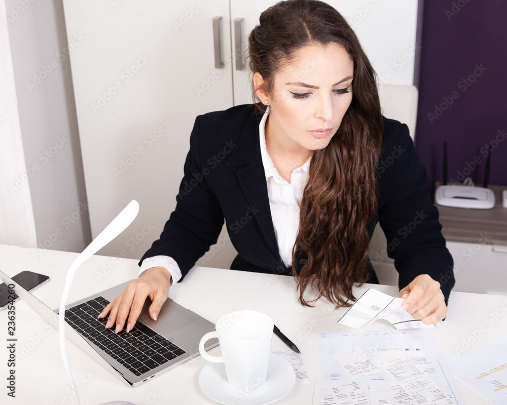 Young attractive business woman working at desk sorting receipts doing expenses paperwork Young attractive business woman working at desk sorting receipts doing expenses paperwork