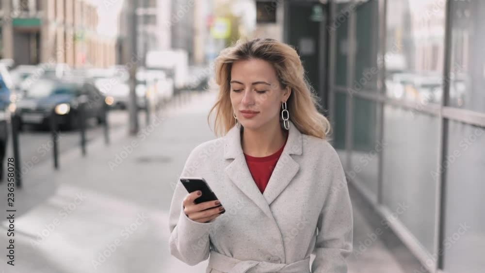 Beautiful blonde woman in white walking and web surfing Beautiful blonde woman in white walking and web surfing