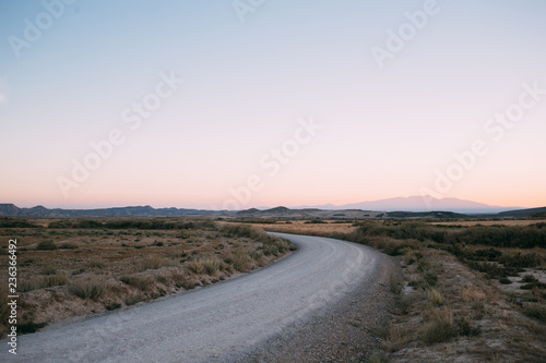Soft pink romantic sunset over deserted empty dry land. Lonely gravel road leads into desert. Wild west concept or amazing travel destinations for vacation in sahara or mexico