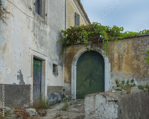Fototapeta Naklejka Na Ścianę i Meble -  Shabby old house with flaking facade and green door at narrow street and stairs, vintage look, Corfu Greece