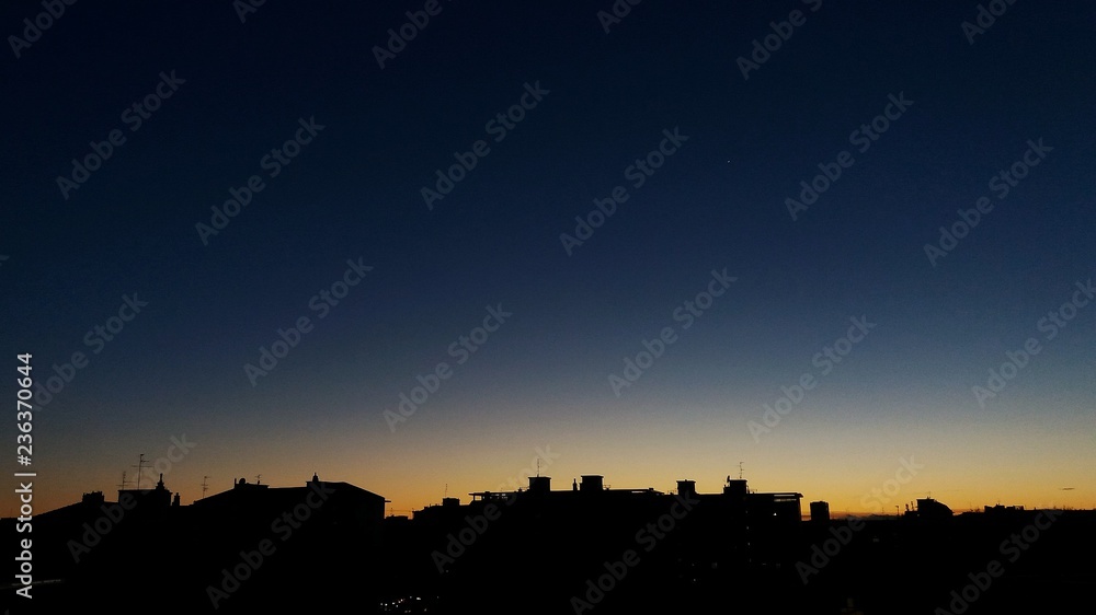 Blue to yellow gradient clear sky sunset with building silhouettes. Minimalist early evening city skyline with copy space for text, advertising message, song lyrics