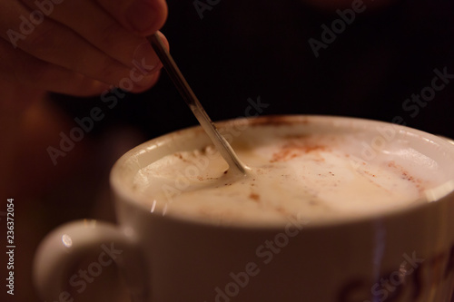 A man's hand mixing with spoon of latte