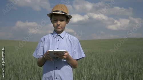 farmer boy in a hat uses a tablet in the field, checks the crop photo