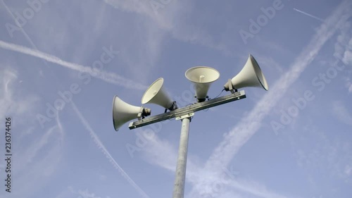 Outdoor public address loudspeakers against a blue sky and trees in slow motion