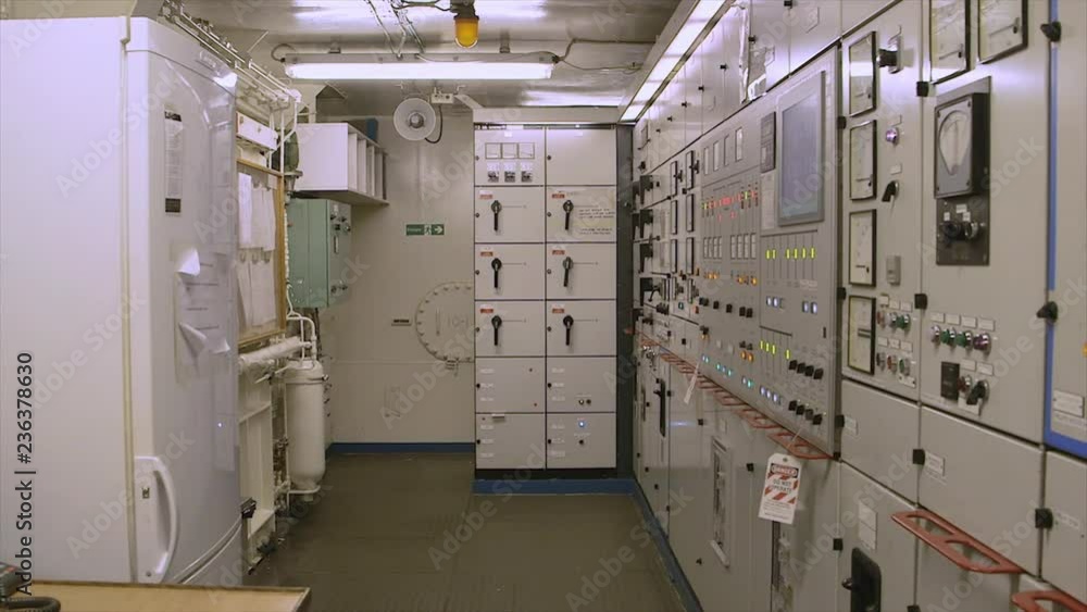 Mid still shot of control room, florescent bright light, emergency monitors, capturing an alarm speaker, monitoring instruments and gauges for different ship engine parameters, control switches, push Mid still shot of control room, florescent bright light, emergency monitors, capturing an alarm speaker, monitoring instruments and gauges for different ship engine parameters, control switches, push