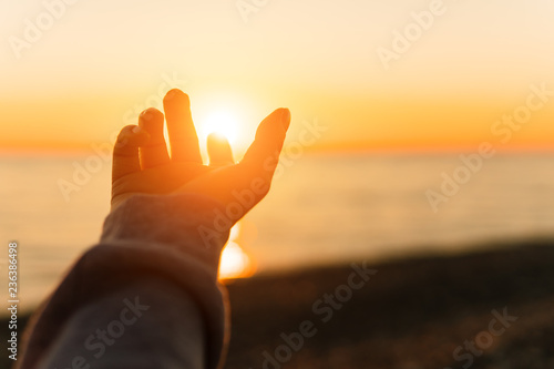Hand reaching for sun. Sunset sun over the sea.