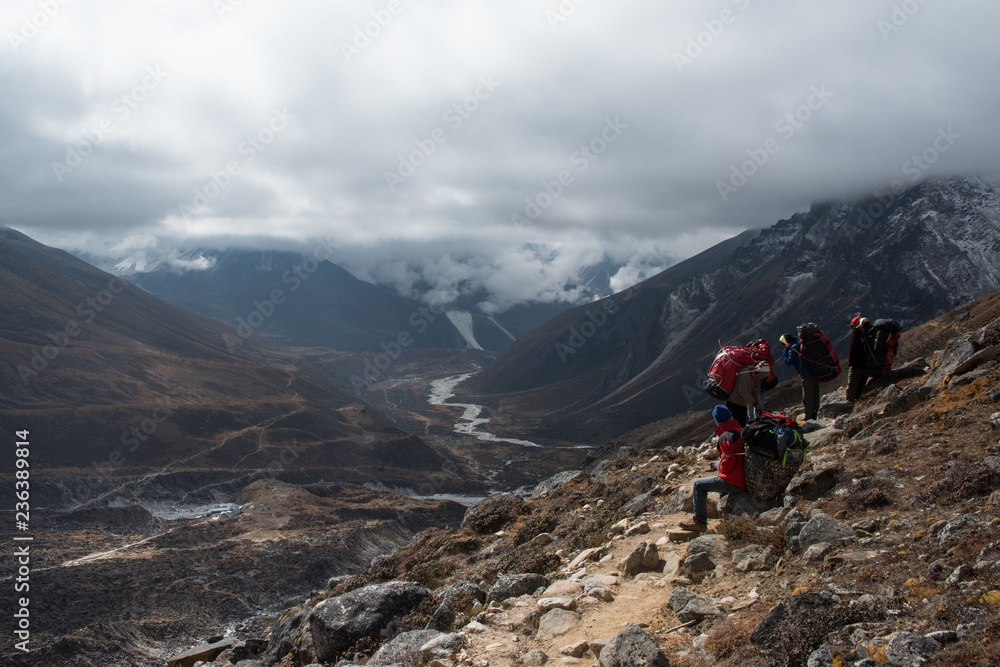 Nepalese porter carrying large loads of bags on his back along a track from Lobuche to Gokyo on Everest base camp trekking route,Nepal